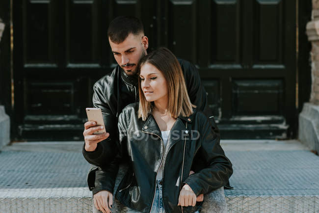 Embracing couple browsing smartphone at street — Stock Photo