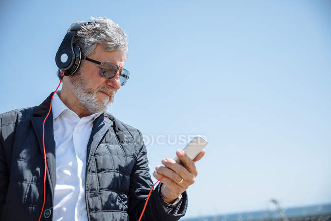 Uomo anziano con cuffie e smartphone — Foto stock