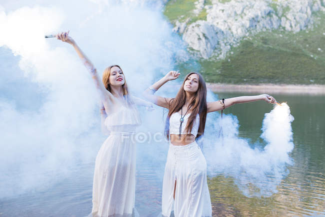 Two girls with flares posing at lake — Stock Photo