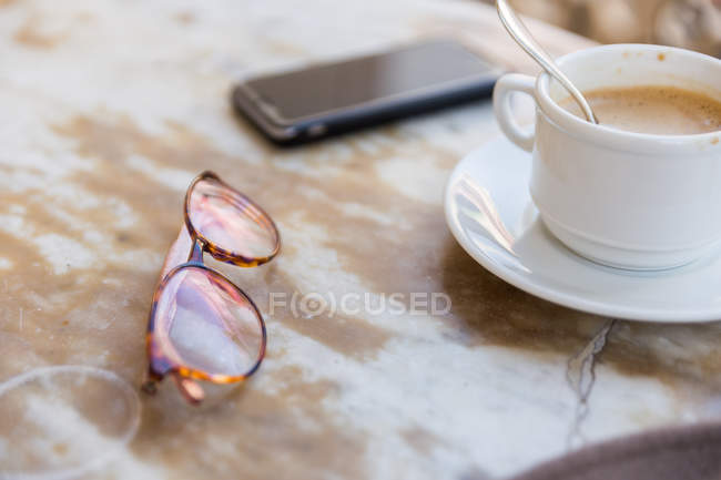 Крупним планом окуляри, телефон і чашка кави — стокове фото