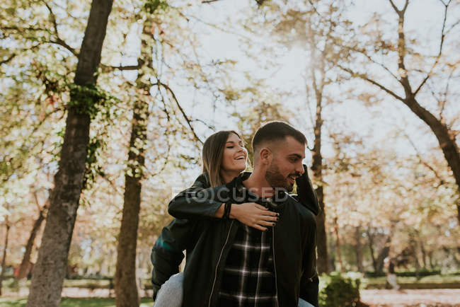 Hombre joven montando chica en la espalda en el parque de otoño - foto de stock