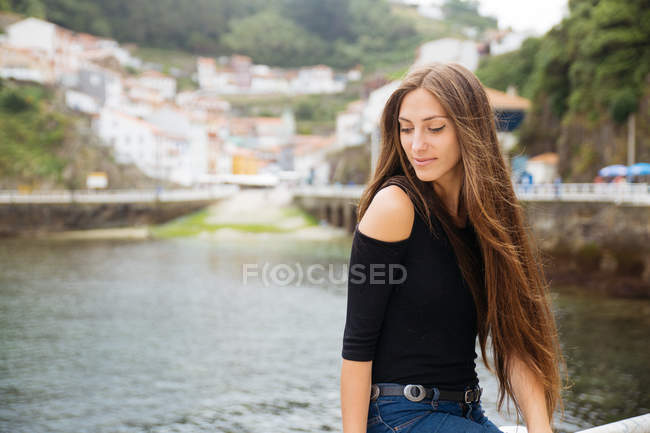 Portrait of young woman with long hair against of river near town — Stock Photo