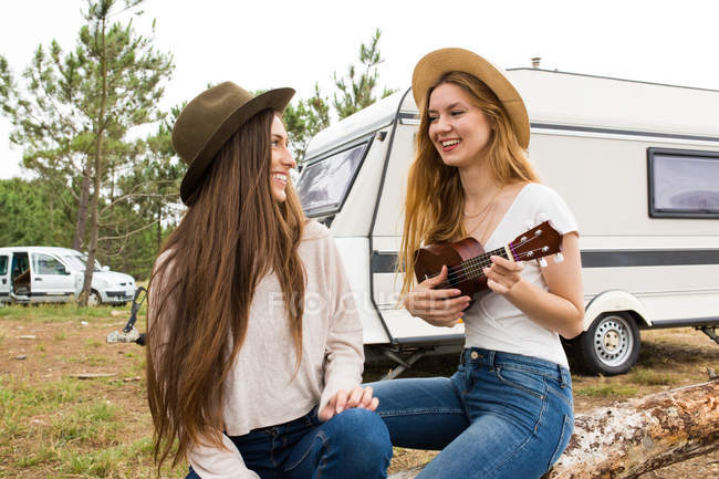 Due ragazze sedute su legno e giocare ukulele — Foto stock