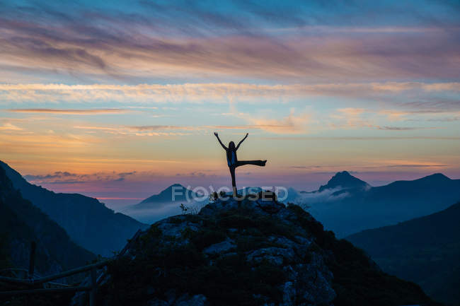 Silueta de turismo animando puesta de sol en la cima de la montaña contra de cielo increíble - foto de stock
