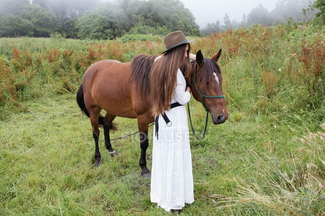 Giovane ragazza in abito bianco accarezzando cavallo — Foto stock