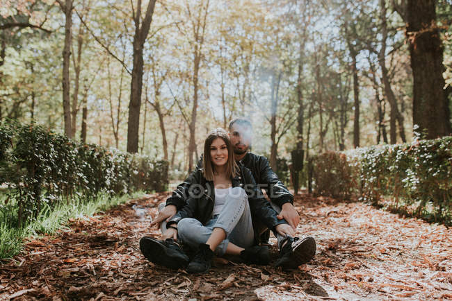 Молода пара сидить на землі на парковій алеї і дивиться на камеру — стокове фото