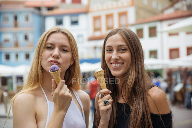 Retrato de dos chicas sonrientes con helado posando sobre edificios sobre fondo - foto de stock