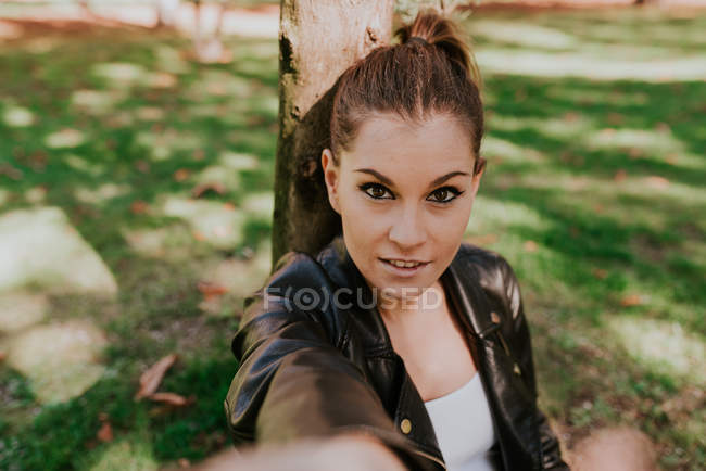 Portrait of young girl sitting at park and outstretching arm at camera — Stock Photo