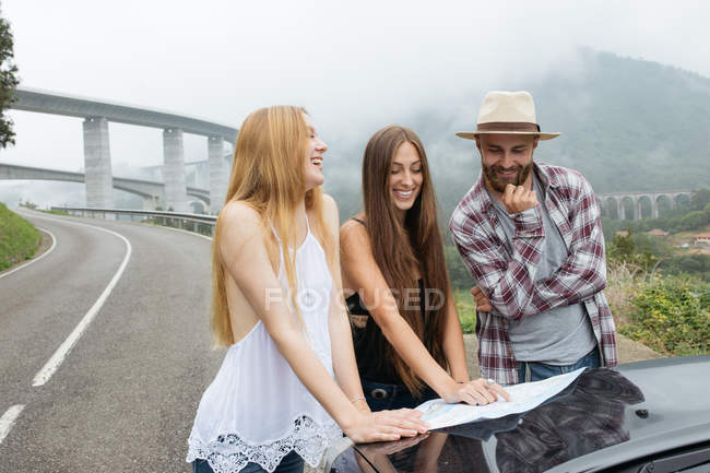 Dos chicas y un hombre mirando en el mapa en la carretera - foto de stock