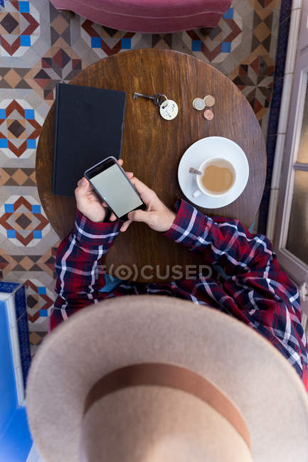 Male in hat using phone at table — Stock Photo