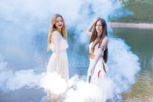 Two girls with flares dancing at lake — Stock Photo