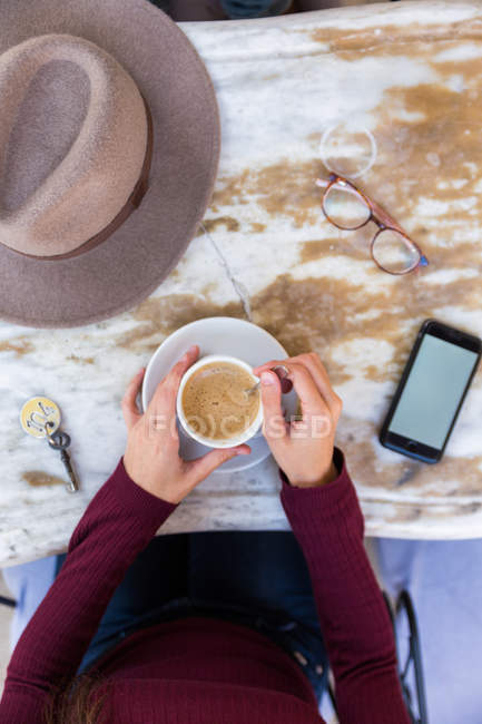 Feminino segurando telefone e café na mesa — Fotografia de Stock