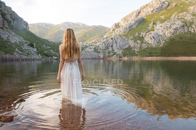 Backview of woman standing in mountain lake in white dress — Stock Photo