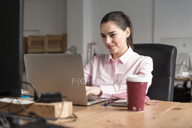 Брюнетка бізнес-леді набравши на ноутбуці в офіс на робочому місці — стокове фото