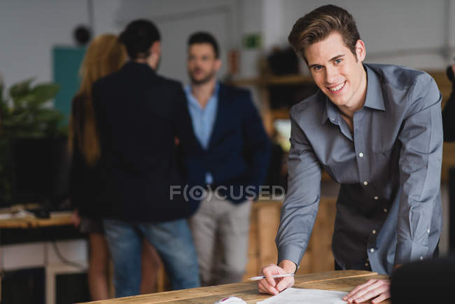 Porträt eines Mannes, der Papiere unterschreibt und im modernen Büro in die Kamera blickt — Stockfoto