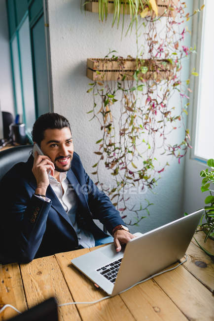 Portrait of businessman browsing laptop and having phone conversation — Stock Photo