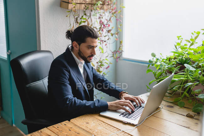 Stylish office worker wearing suit typing on his laptop sitting at the workplace. Horizontal indoors shot. — Stock Photo