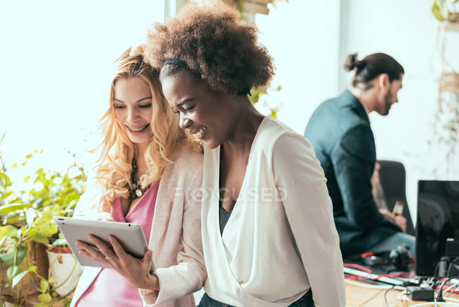 Women laughing with tablet in hands at modern office — Stock Photo