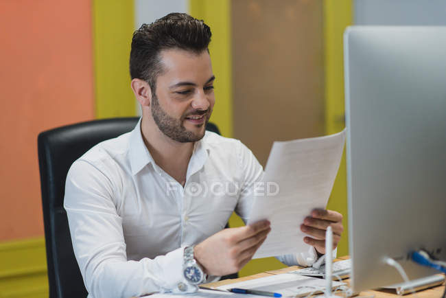 Retrato del hombre de negocios sentado en el lugar de trabajo y mirando los papeles - foto de stock