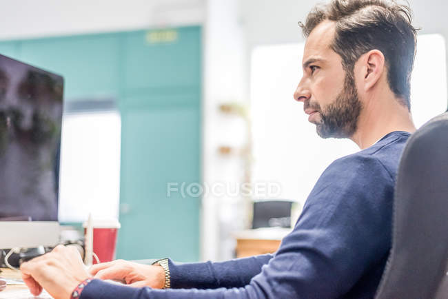 Vista lateral do homem pensativo usando PC no local de trabalho do escritório — Fotografia de Stock