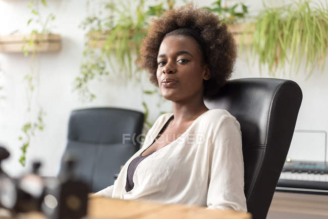 Молода жінка сидить на робочому місці в офісному кріслі і дивиться на камеру — стокове фото