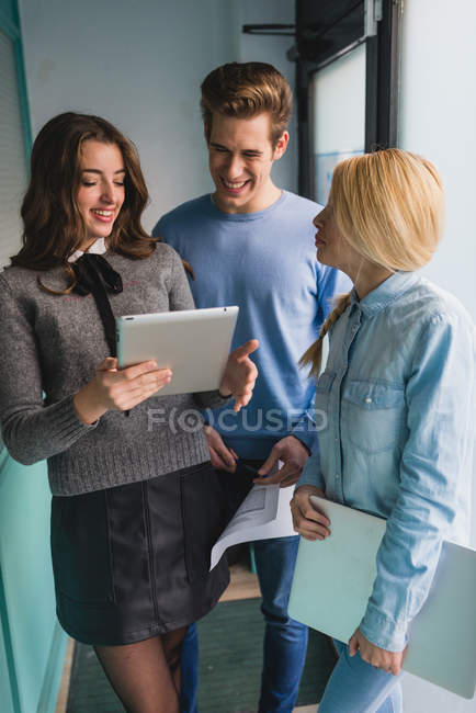 Портрет улыбающейся девушки, показывающей табличку коллегам в офисном коридоре — стоковое фото