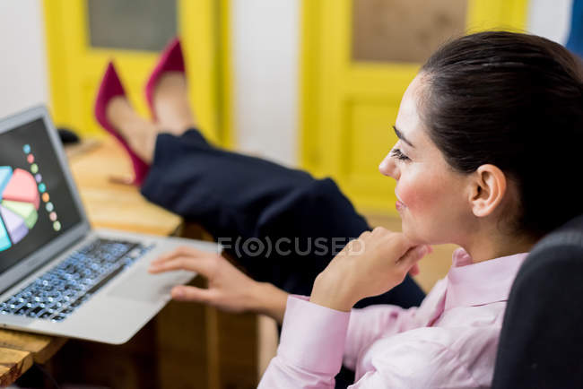 Вид збоку жінка з ноги на столі, дивлячись на діаграму на ноутбук. — стокове фото