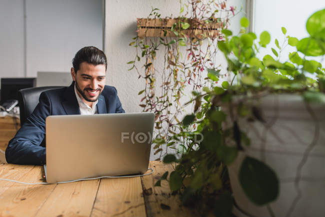 Retrato del hombre de negocios sentado en la mesa y el uso de la computadora portátil en el lugar de trabajo - foto de stock