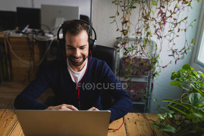 Portrait of man in headphones sitting at table and using laptop at office workplace — Stock Photo