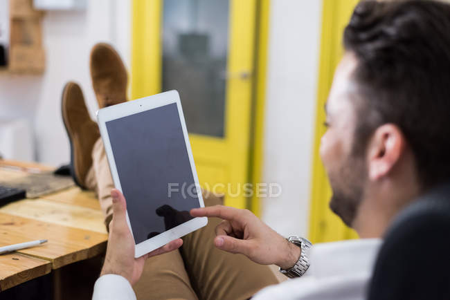 Over shoulder view of man with legs on table browsing tablet. — Stock Photo