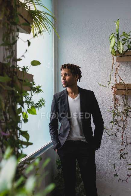Portrait of businessman in suit posing near window with potted plants — Stock Photo