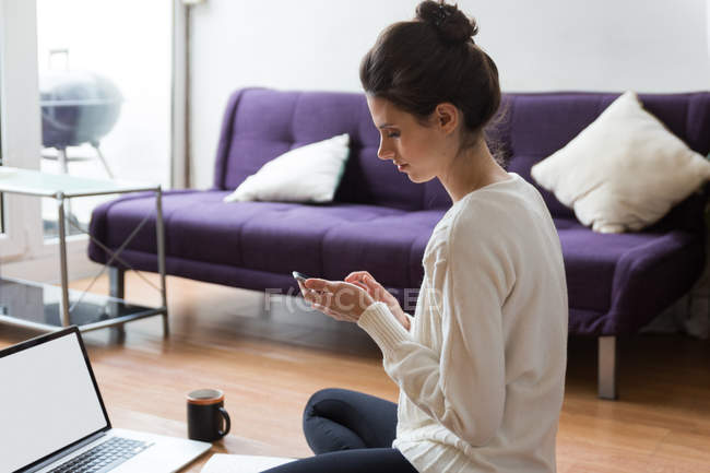 Vista laterale della ragazza bruna seduta sul pavimento con laptop e smartphone di navigazione — Foto stock