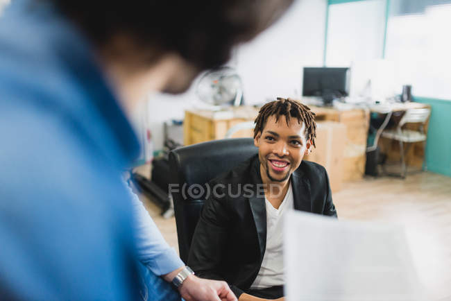 Vista sobre el hombro del hombre sonriente mirando a su colega en la oficina . - foto de stock