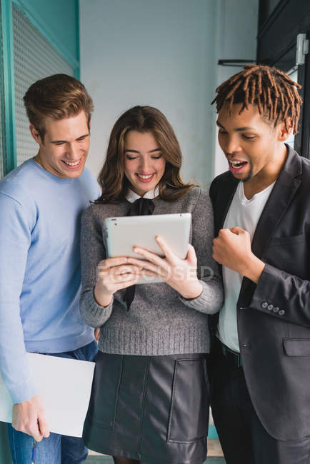 Portrait of laughing colleagues looking at tablet in office corridor — Stock Photo