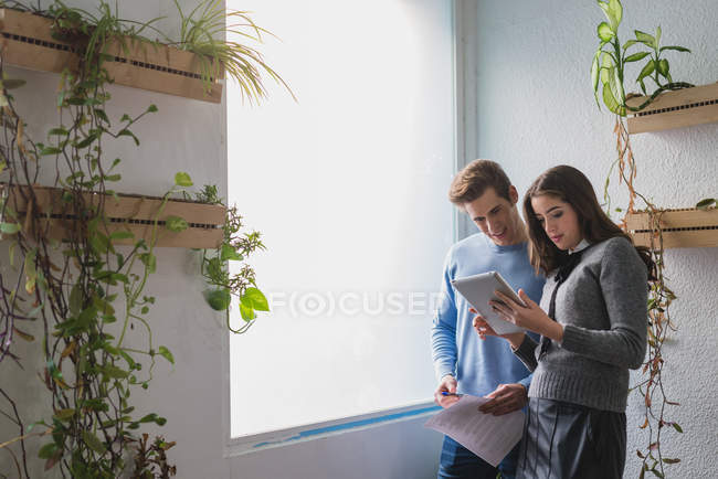 Portrait of man and woman standing near window and looking at tablet screen — Stock Photo