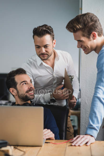 Portrait d'un homme assis à table et montrant un écran d'ordinateur portable à ses collègues — Photo de stock