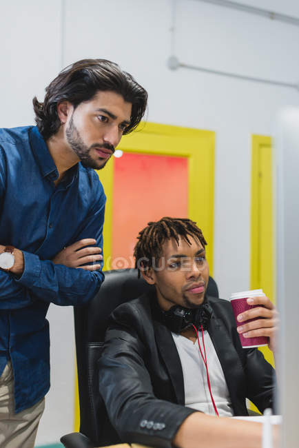 Retrato del hombre de negocios mirando a los colegas pantalla de ordenador en el lugar de trabajo - foto de stock