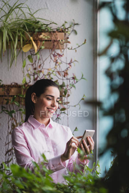 Porträt einer Geschäftsfrau, die am Fenster steht und auf ihrem Smartphone surft — Stockfoto