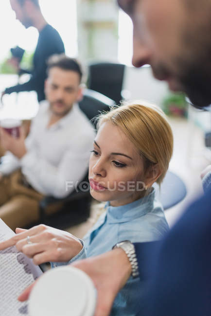 Über-die-Schulter-Ansicht eines blonden Mädchens, das beim täglichen Bürogespräch mit dem Finger auf die Papiere von Kollegen zeigt — Stockfoto