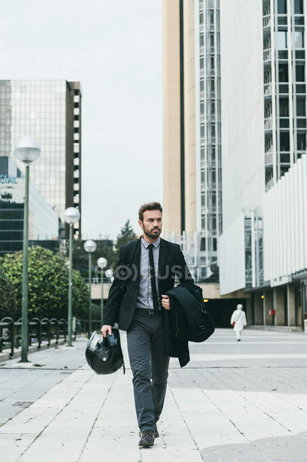 Элегантный бизнесмен прогуливается с мотоциклетным шлемом — стоковое фото