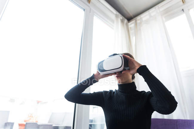 Mujer sentada en un sofá morado y sosteniendo auriculares VR - foto de stock