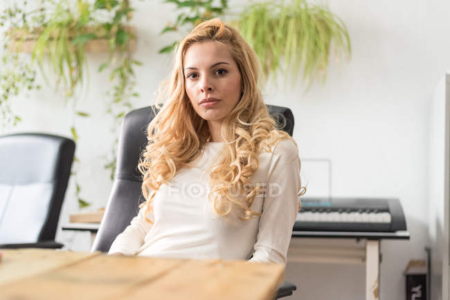 Задумчивая блондинка-бизнесмен сидит на рабочем месте и смотрит в камеру — стоковое фото