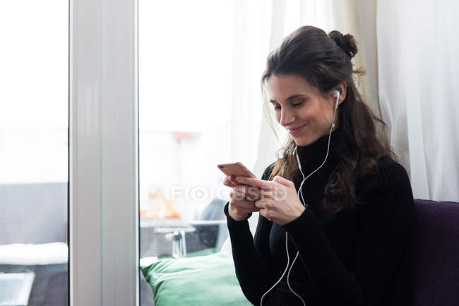 Ritratto di ragazza sorridente che indossa gli auricolari e chatta sullo smartphone — Foto stock