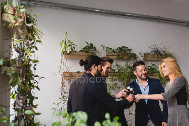 Happy coworkers clanging beer bottles in office after working time — Stock Photo