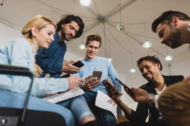 Low angle view of office workers looking into smartphones while meeting at office — Stock Photo