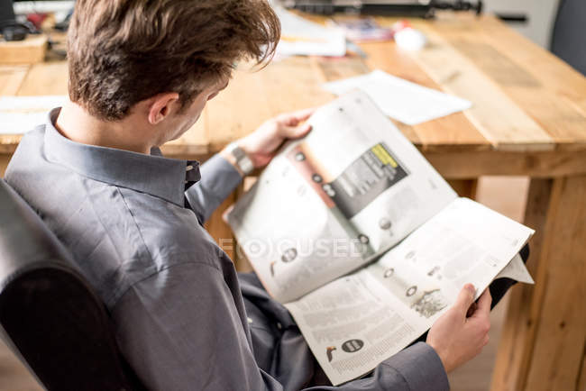 Vue arrière d'un homme d'affaires lisant un journal assis dans une chaise de bureau . — Photo de stock