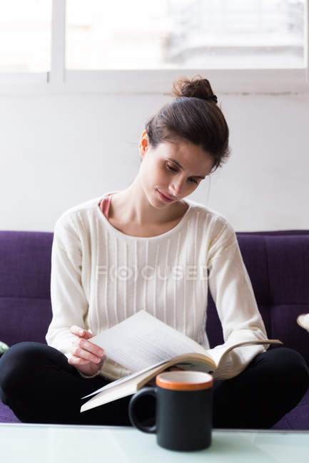 Brünette Frau sitzt auf Sofa und liest Buch. — Stockfoto