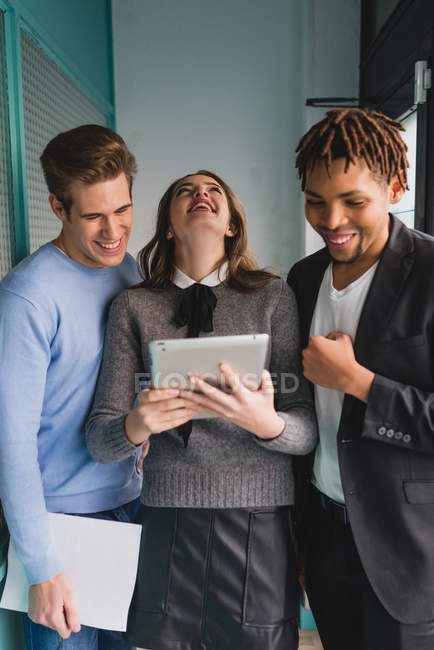 Портрет смеющихся коллег, смотрящих на планшет в офисном коридоре — стоковое фото
