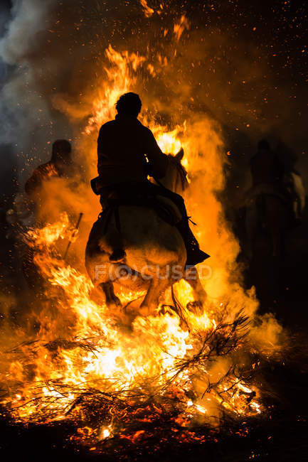 Vista lateral del caballo montando a través de una hoguera en un ritual de purificación - foto de stock
