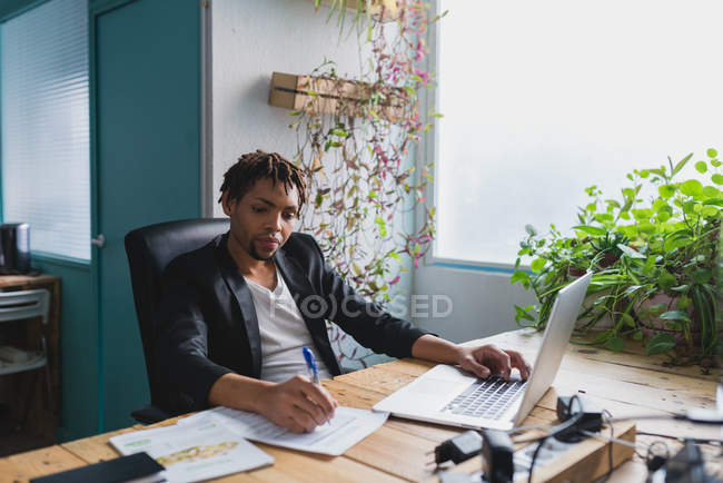 Portrait of man using laptop and doing paperworks at workplace in modern office — Stock Photo